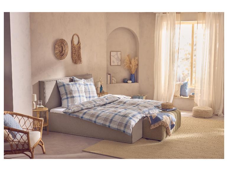 Slaapkamer met tweepersoonsbed, blauw-beige geruit beddengoed en rieten wanddecoraties.