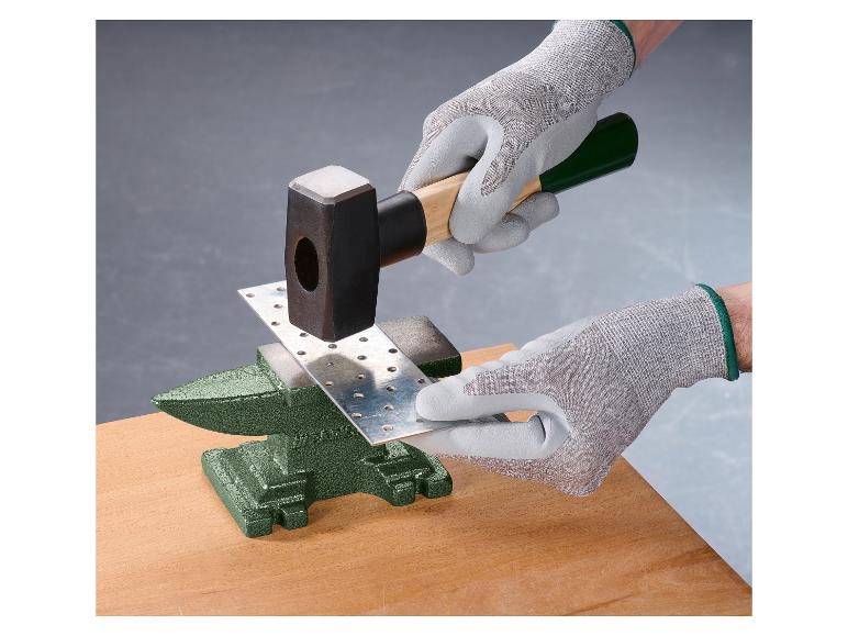 Handen in handschoenen hameren een metalen plaat op een aambeeld.