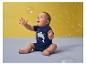 Baby in blauw haaien-T-shirt speelt met zeepbellen tegen een gele achtergrond.