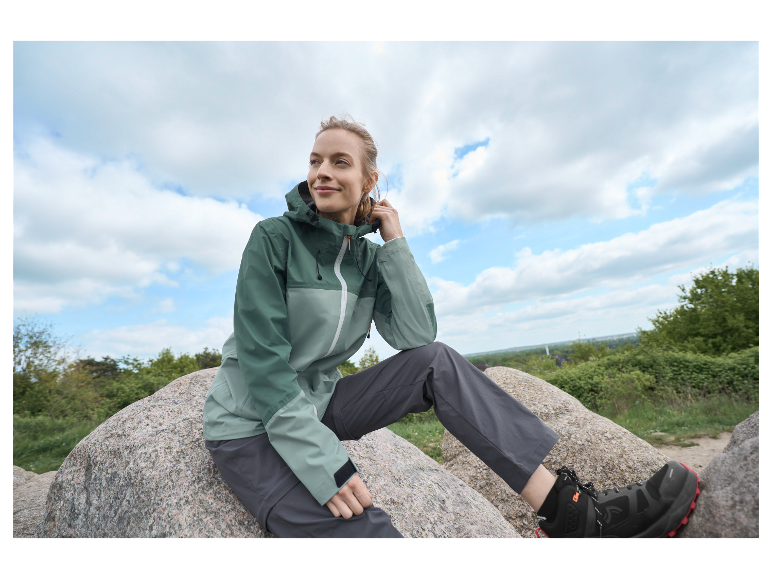 Vrouw zit op een rots in een sportjas en broek.