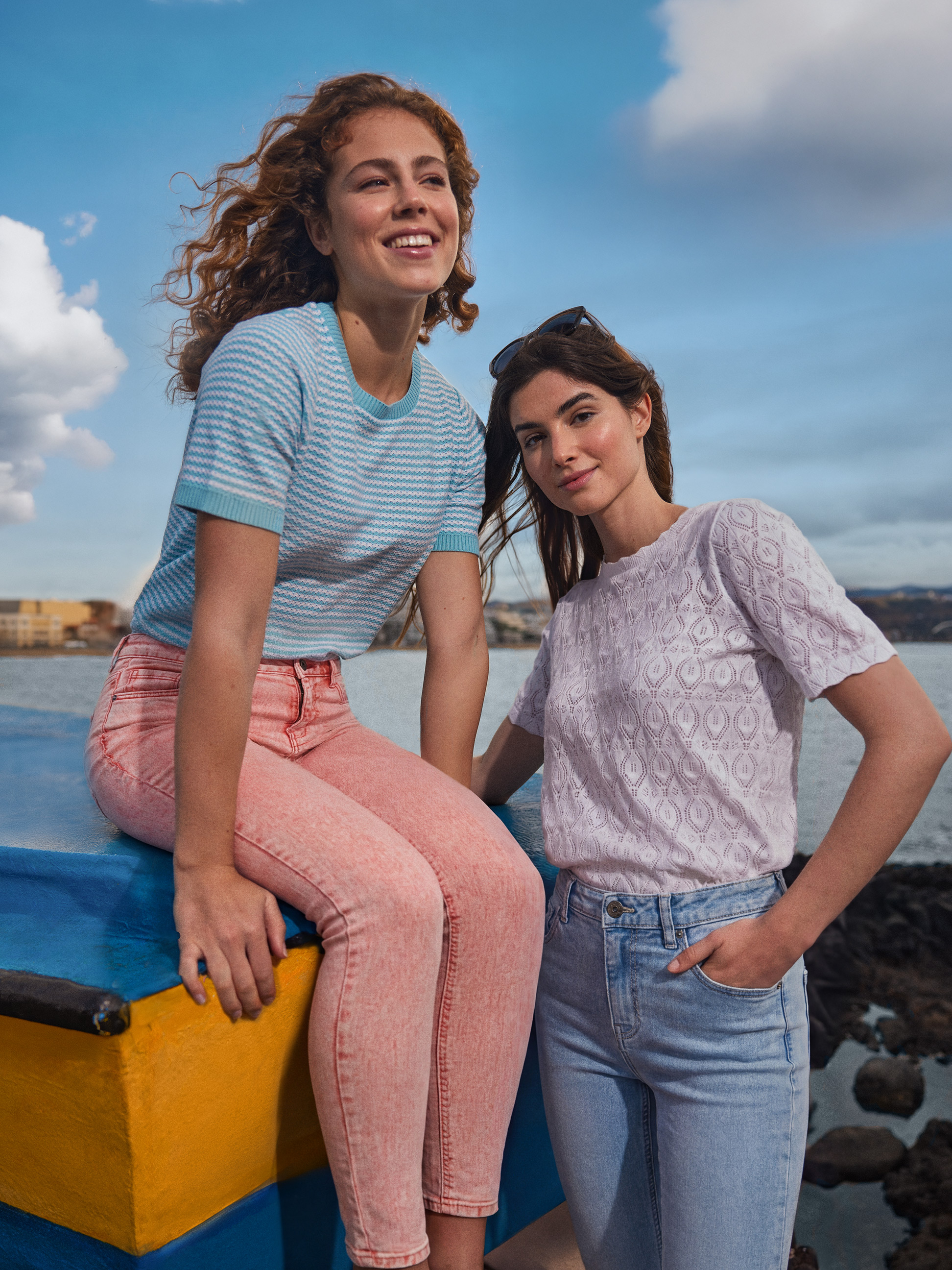 Twee vrouwen in zomerjeans en gebreide tops poseren bij de zee.