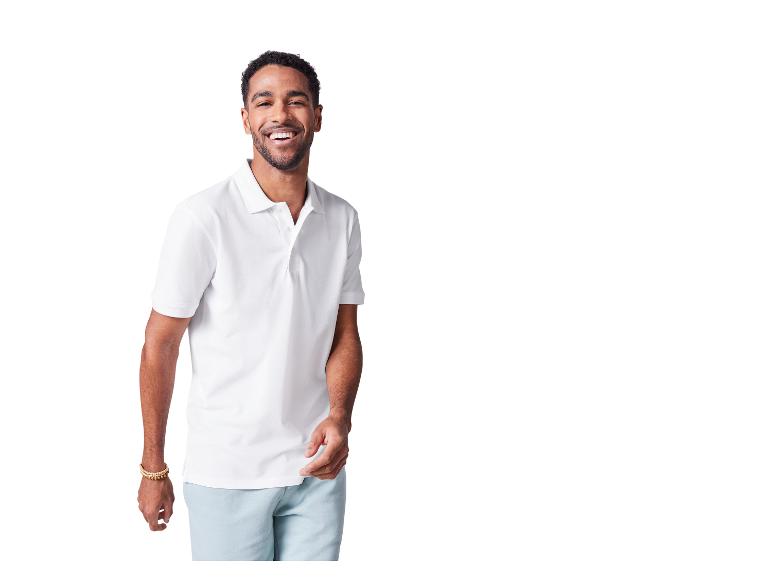 Een lachende man draagt een wit poloshirt en een lichtblauwe broek.