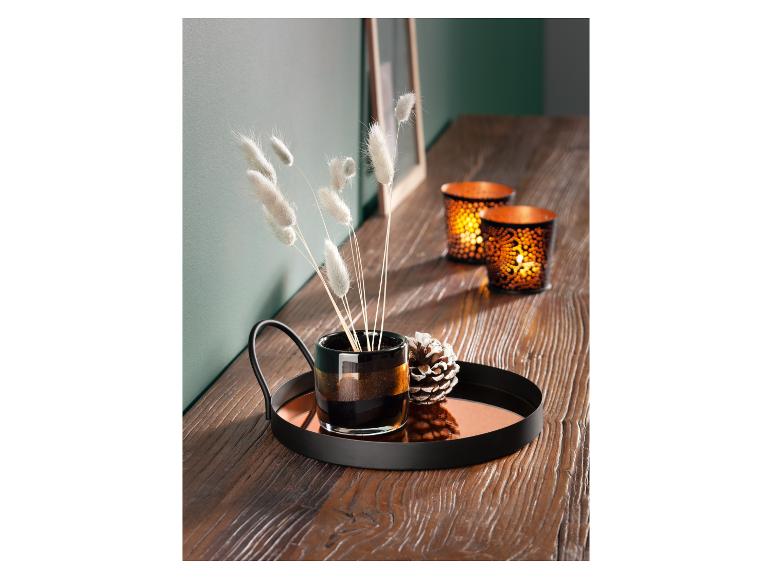 Een zwarte dienblad met een glazen vaas, kaarsen en decoratieve dennenappels.