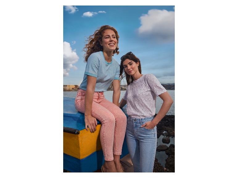 Twee vrouwen in casual tops en jeans bij het water, één in een gestreepte top en roze jeans, de andere in een patroon top en lichtblauwe jeans.