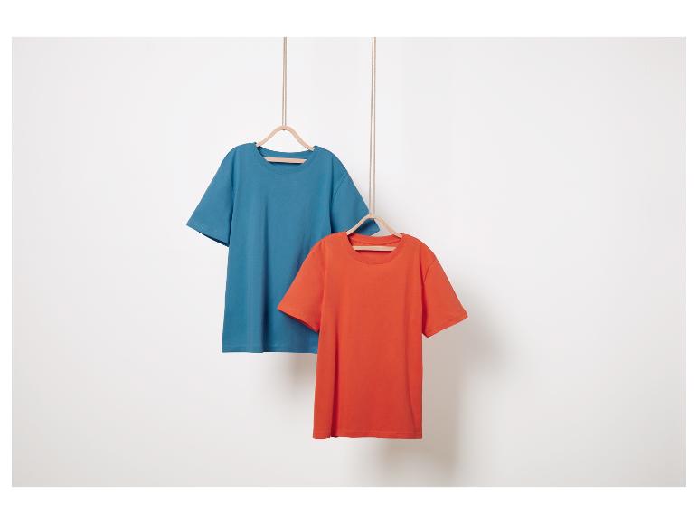 Twee effen t-shirts, blauw en oranje, hangen aan houten hangers.