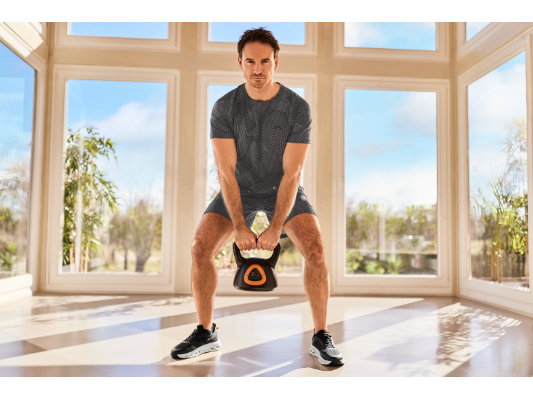 Man in sportkleding traint met een kettlebell in een lichte kamer.