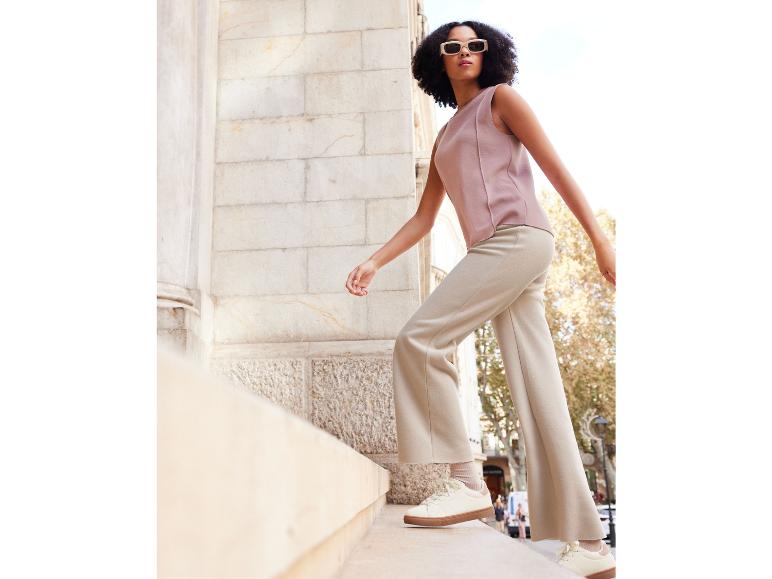 Een vrouw draagt beige broek en witte sneakers, staand op een traptrede.