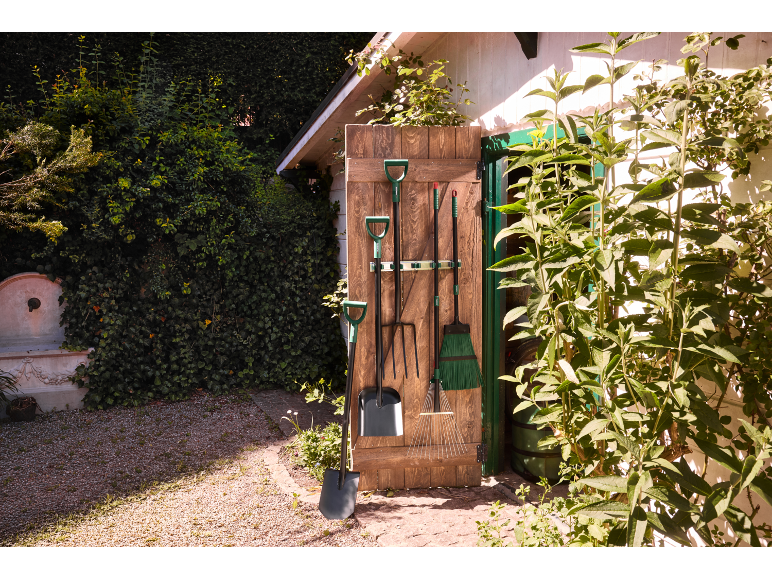 Tuin gereedschap hangend aan een houten deur, met een schop en hark op de voorgrond.