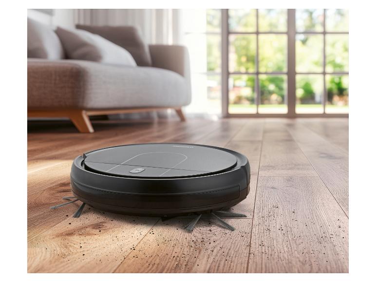 Robotstofzuiger op houten vloer met vuil, in een woonkamer.