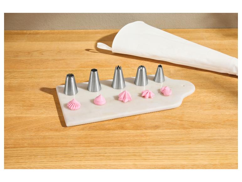 Spuitmondjesset met roze glazuur op een marmeren plank en een spuitzak.