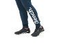 Persoon draagt donkerblauwe joggingbroek met wit logo en zwarte sportschoenen.