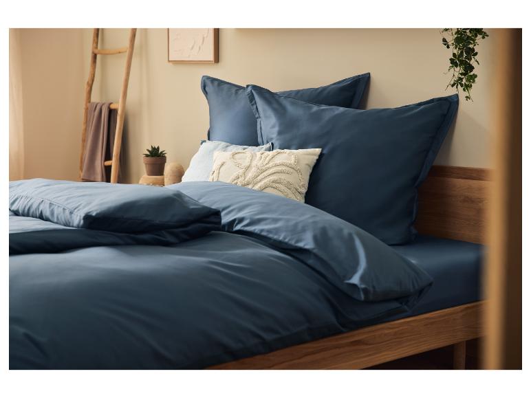 Marineblauwe beddengoed op een houten bed met decoratieve kussens en planten.