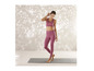 Een vrouw in roze sportbeha en leggings staat op een yoga mat.