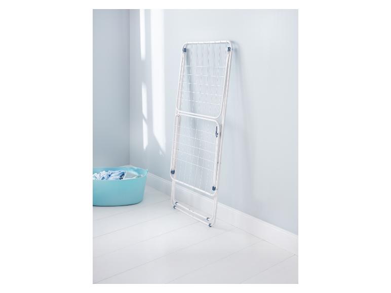 Wit wasrek leunend tegen een lichtblauwe muur met een wasmand op de vloer.