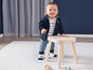 Een baby in een blauwe trui en broek staat op een houten krukje.