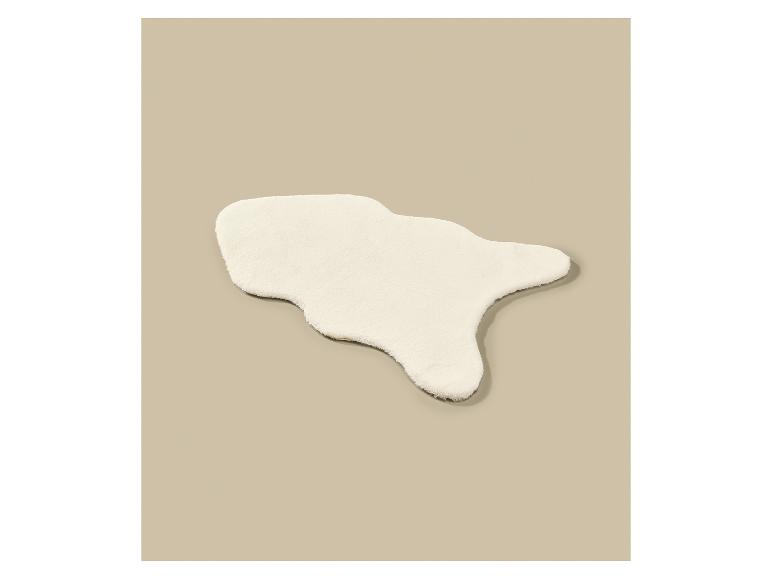 Een wit, pluizig, onregelmatig gevormd vloerkleed op een beige achtergrond.