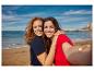 Twee lachende vrouwen in T-shirts op het strand, nemen een selfie.