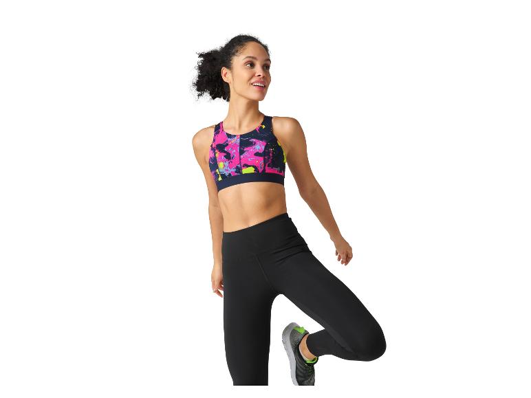 Een vrouw in een kleurrijke sportbeha en zwarte leggings rekt zich uit.