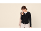 Lachende vrouw in zwart vest, wit T-shirt en beige trenchcoat over haar schouder.