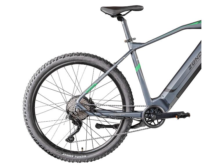 Achteraanzicht van een grijze elektrische mountainbike met groene accenten, met een band met noppenprofiel en zichtbare aandrijflijn.