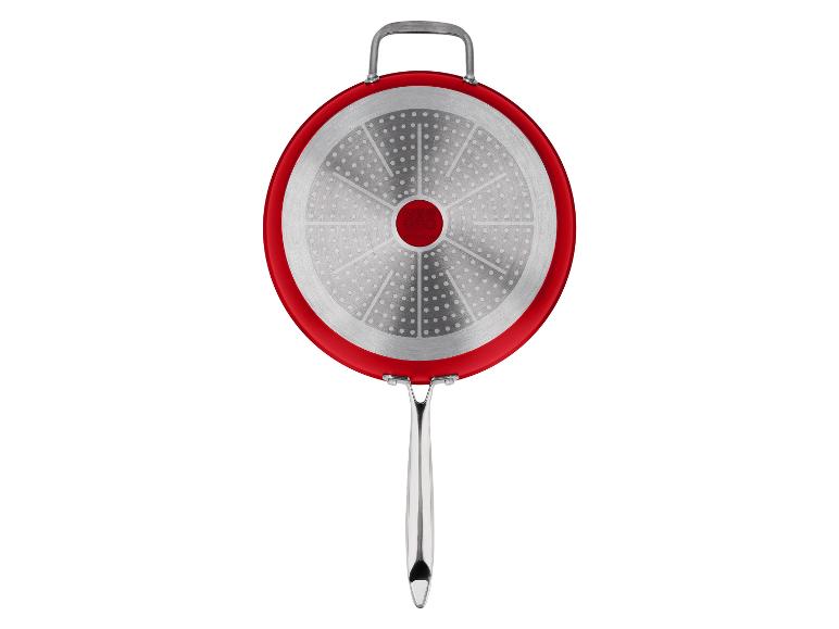 Onderkant van een rode koekenpan met zilveren inductiebodem en metalen handvat.