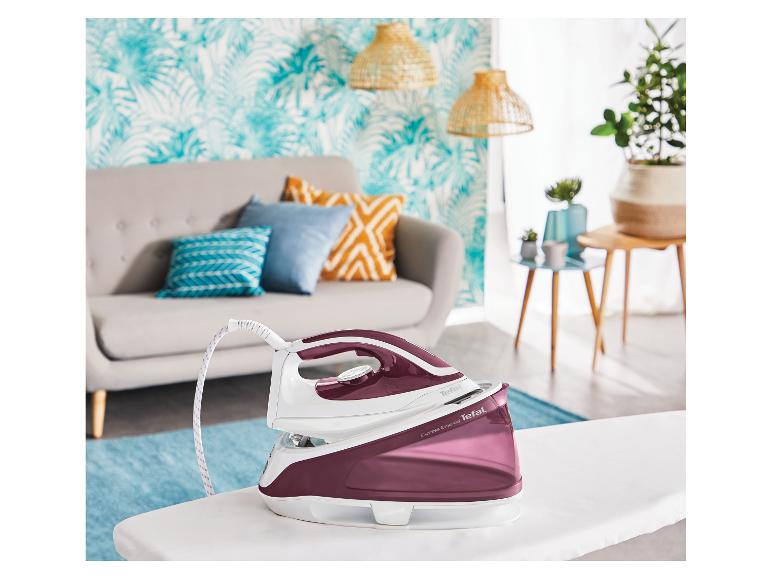 Stoomstrijkijzer op een strijkplank in een woonkamer met bank en planten.