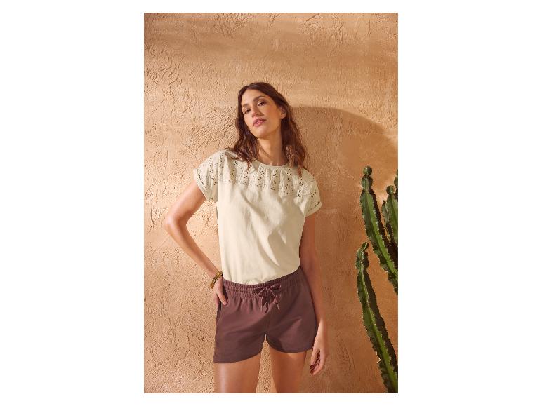 Vrouw in geborduurd T-shirt met korte mouwen en bruine shorts met trekkoord.