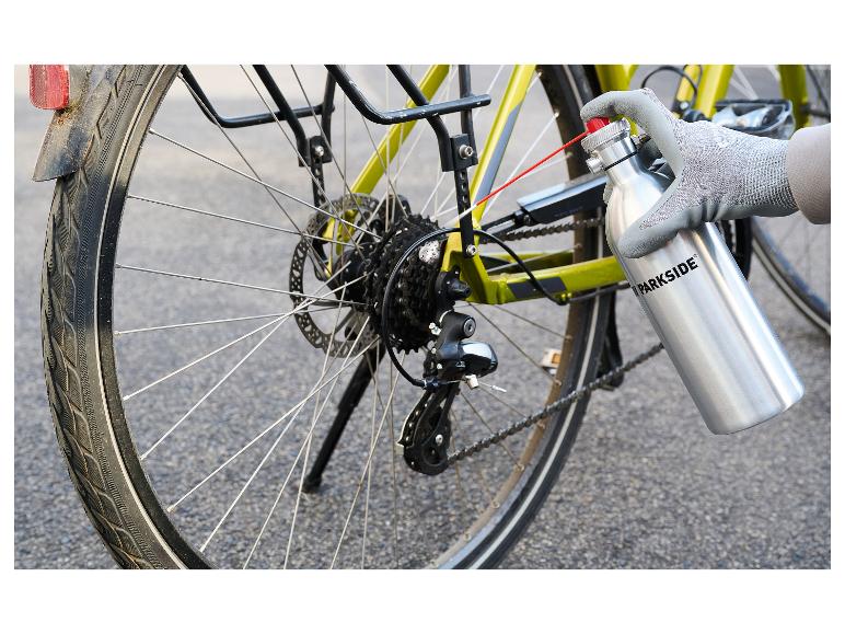 Hand in handschoen smeert een fietsketting met een spuitfles.