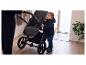 Kind in donkerblauwe jas houdt kinderwagen vast, naast een volwassene.