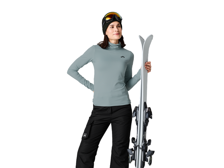 Vrouw in skikleding met ski's, skibril en muts.