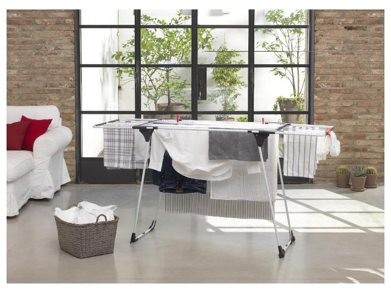 Wasrek met kleding in een lichte woonkamer met bank en planten.