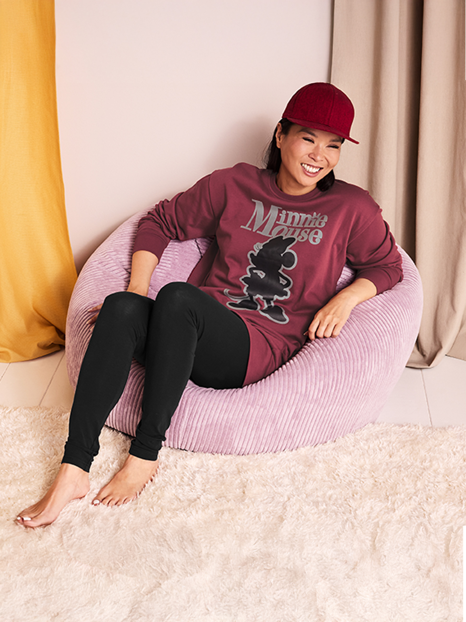 Vrouw in Minnie Mouse-pyjama en pet zit in een roze zitzak.