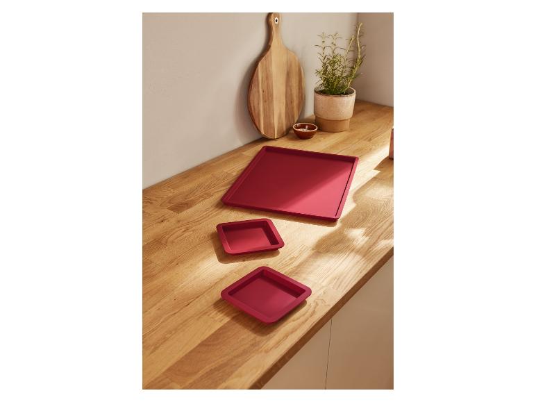 Drie vierkante rode dienbladen op een houten oppervlak.