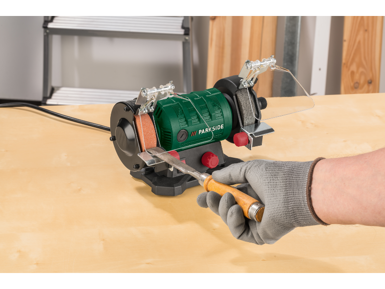 Groene bankslijpmachine met een houtbeitel die wordt geslepen door een gehandschoende hand.