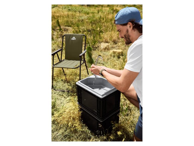 Man wast handen bij een draagbare gootsteen met een campingstoel op de achtergrond.