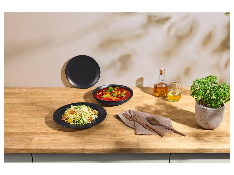 Borden pasta en soep in zwarte kommen, met koperen bestek en olie op een houten tafel.