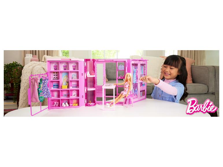 Meisje speelt met roze poppenkast, pop en accessoires op een witte tafel.
