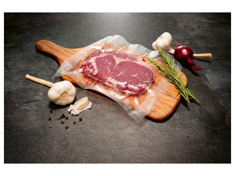 Vacuümverpakte biefstuk met knoflook, rode ui en rozemarijn op een houten plank.