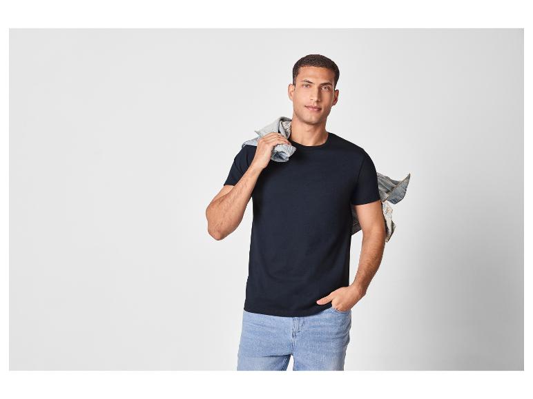 Man in een zwart T-shirt en lichtblauwe jeans, met een spijkerjack over zijn schouder.