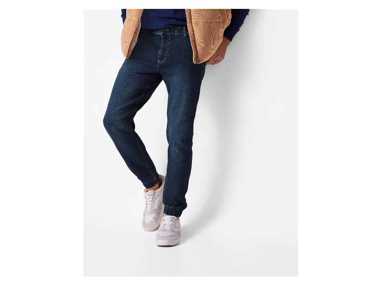 Donkerblauwe jeans met boordjes en witte sneakers.