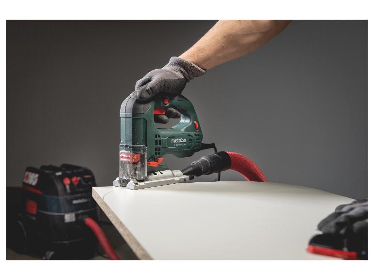 Metabo decoupeerzaag zaagt hout, aangesloten op stofzuiger, hand met werkhandschoen.