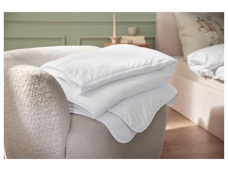 Stapel witte dekbedden op een beige fauteuil in de slaapkamer.