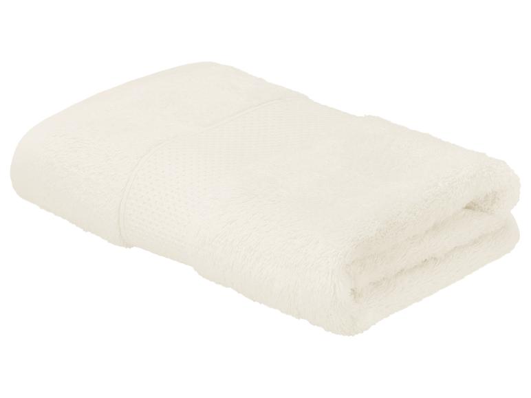 Gevouwen crèmekleurige handdoek met een gestructureerde band, geïsoleerd op een witte achtergrond.