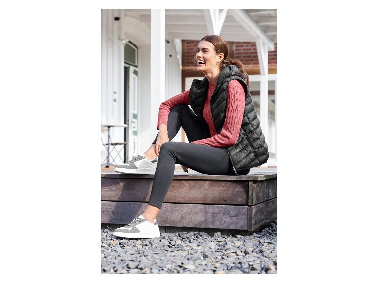 Vrouw draagt zwarte leggings, een zwarte puffer vest en witte sneakers.