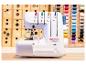 Witte overlock naaimachine met kleurrijke draden, tegen een achtergrond van houten lades.