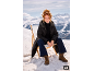 Vrouw in zwarte jas en jeans zittend op een stoel in een besneeuwd berglandschap.