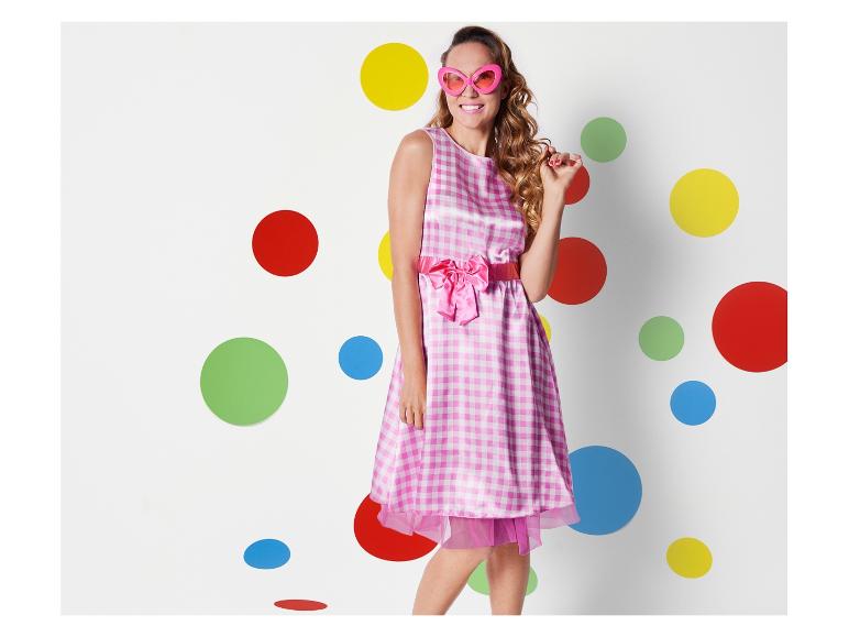 Een vrouw in een roze gebloemde jurk met een roze strik staat voor een achtergrond met kleurrijke stippen.