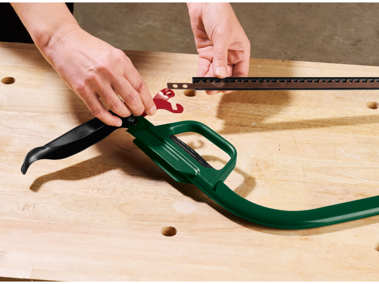 Vrouw monteert een tuinzeg met groen handvat en zwart blad op een houten werkbank.