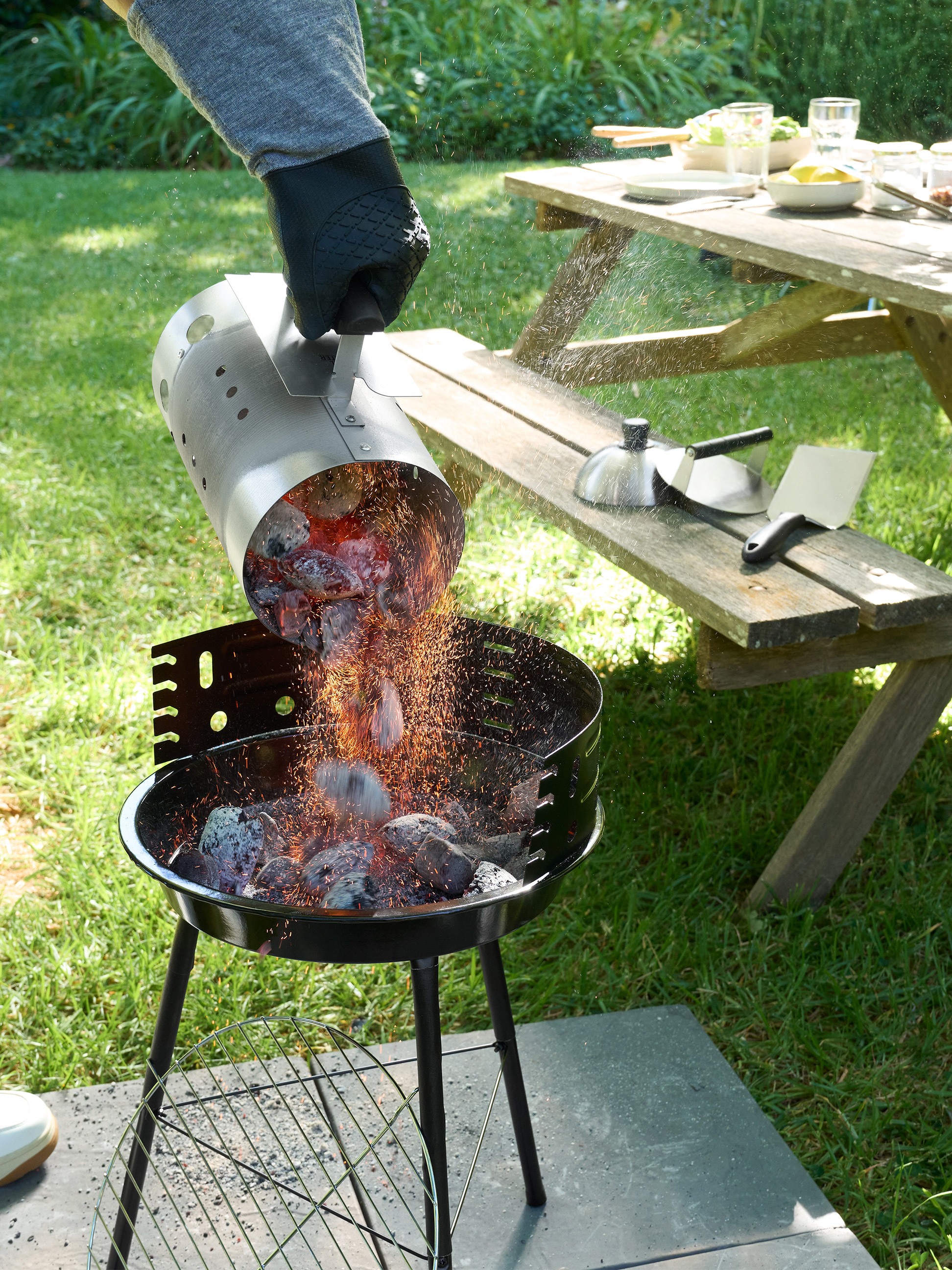 Gloeiende kolen worden uit een brikettenstarter in een houtskoolbarbecue in de tuin gegoten.