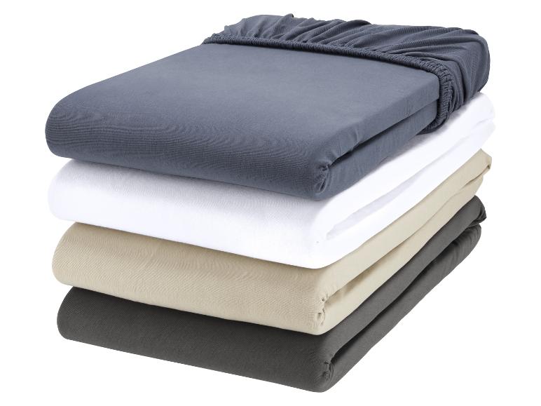 Een stapel van vier jersey hoeslakens in verschillende kleuren.